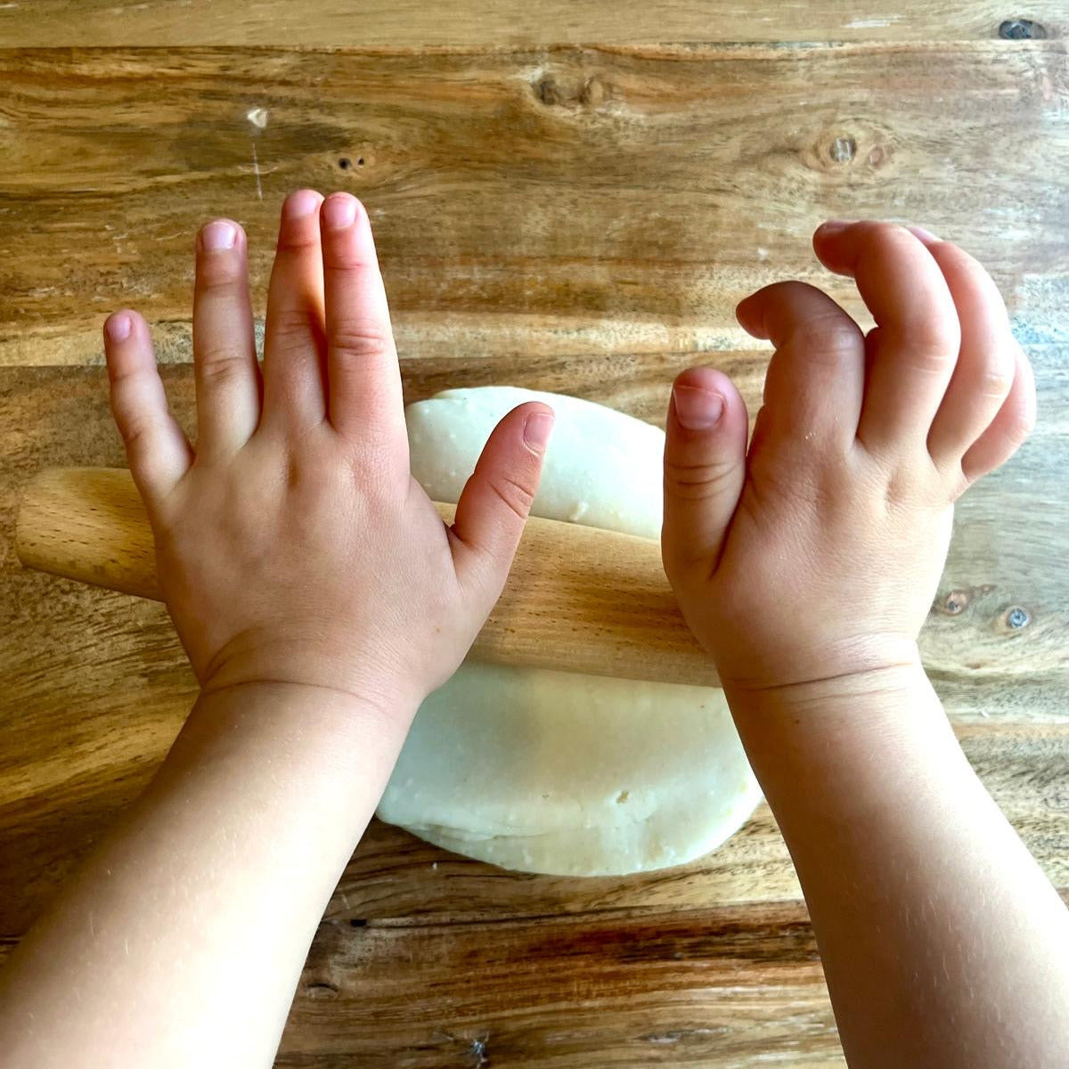 A toddler's hands spreading white play dough using a French style rolling pin