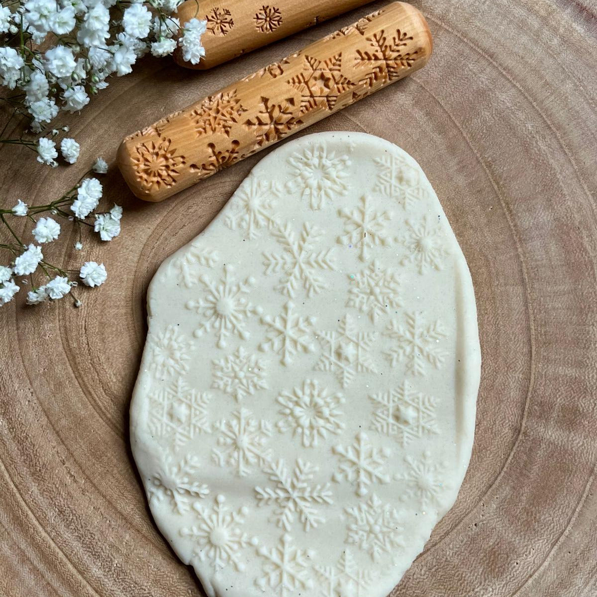 large wooden rolling pin with snowflakes engraved upon it rolled along white playdough